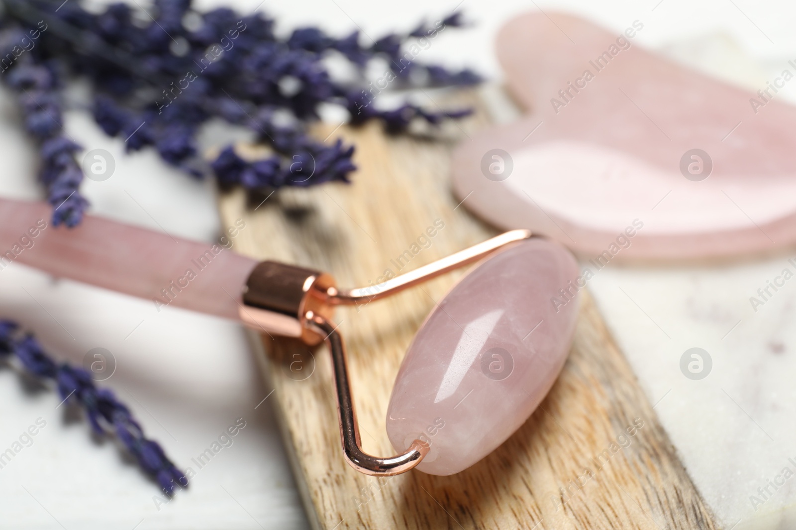 Photo of Face roller, gua sha tool and lavender flowers on light background, closeup