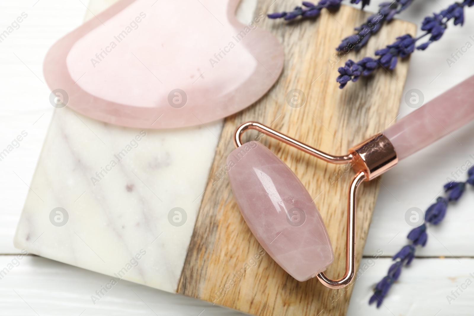 Photo of Face roller, gua sha tool and lavender flowers on white wooden background, closeup