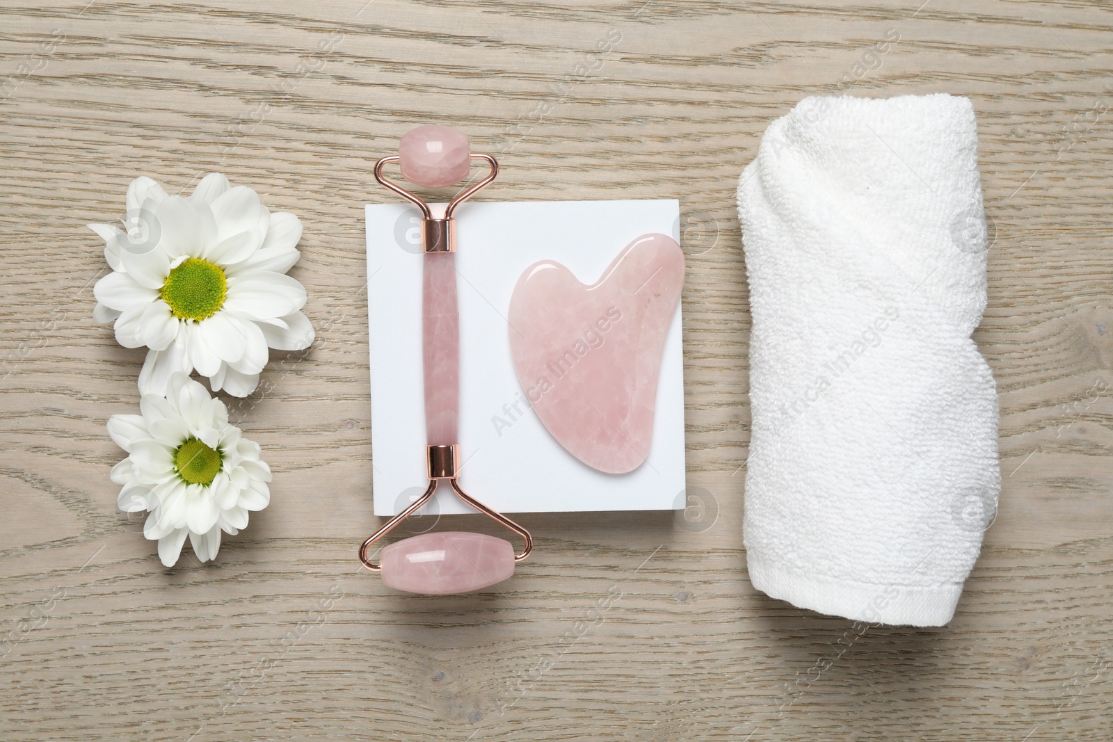 Photo of Face roller, gua sha tool, towel and white chrysanthemum flowers on wooden background, flat lay