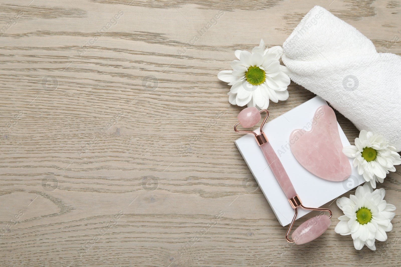 Photo of Face roller, gua sha tool, towel and white chrysanthemum flowers on wooden background, flat lay. Space for text