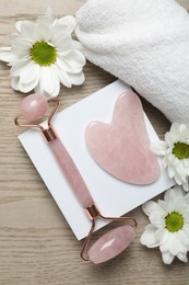 Photo of Face roller, gua sha tool, towel and white chrysanthemum flowers on wooden background, flat lay