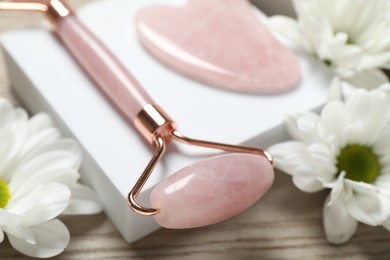 Photo of Face roller, gua sha tool and white chrysanthemum flowers on wooden background, closeup