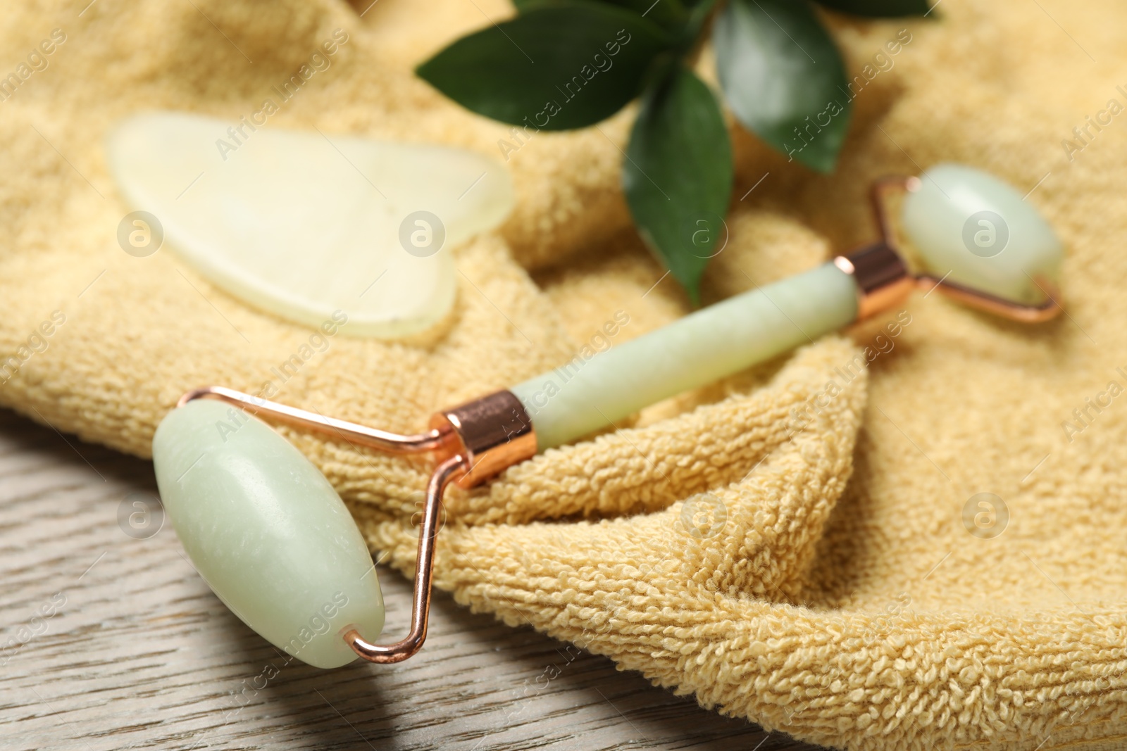 Photo of Face roller, gua sha tool, towel ruscus branch on wooden background, closeup