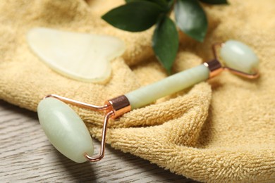 Photo of Face roller, gua sha tool, towel ruscus branch on wooden background, closeup