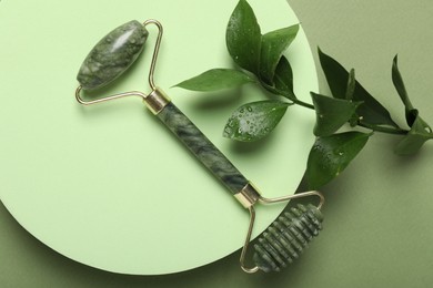 Photo of Face roller and ruscus branch on green background, top view