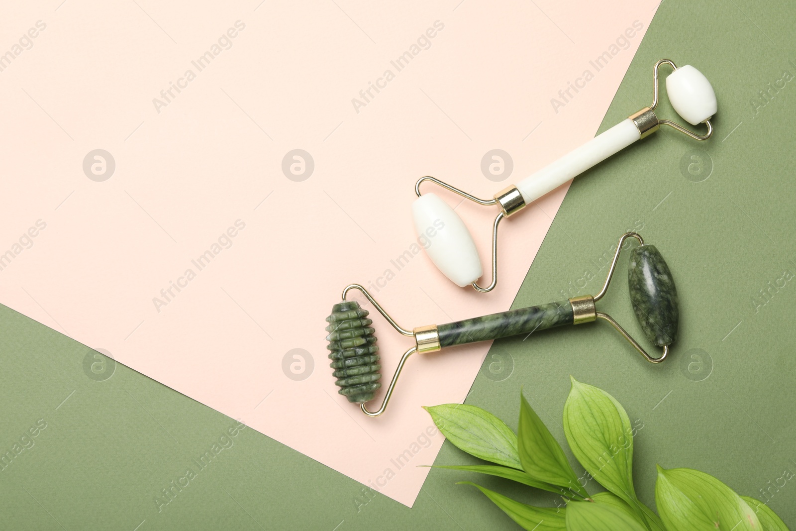 Photo of Face rollers and green leaves on color background, flat lay, space for text