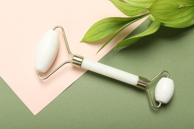 Face roller and green leaves on color background, flat lay