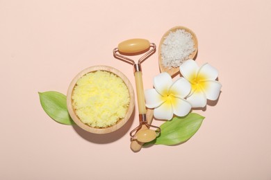 Photo of Face roller, body scrub, sea salt, plumeria flowers and green leaves on beige background, flat lay