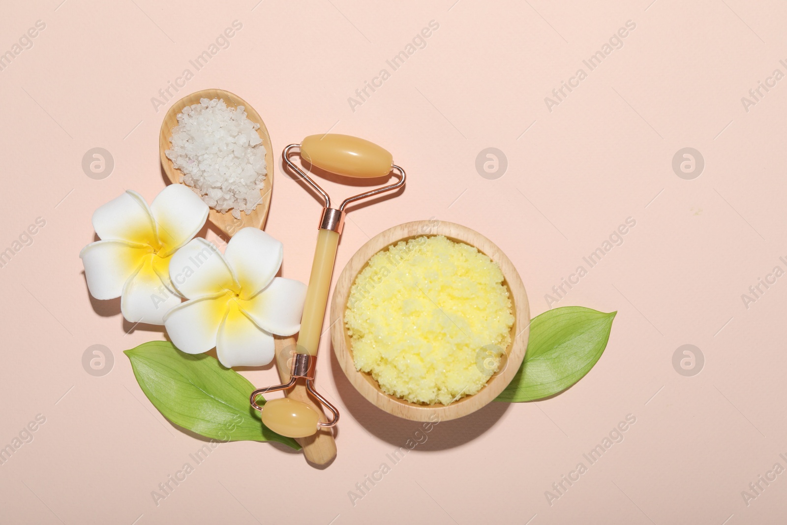 Photo of Face roller, body scrub, sea salt, plumeria flowers and green leaves on beige background, flat lay