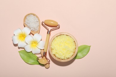 Face roller, body scrub, sea salt, plumeria flowers and green leaves on beige background, flat lay