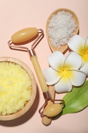 Face roller, body scrub, sea salt, plumeria flowers and green leaf on beige background, flat lay