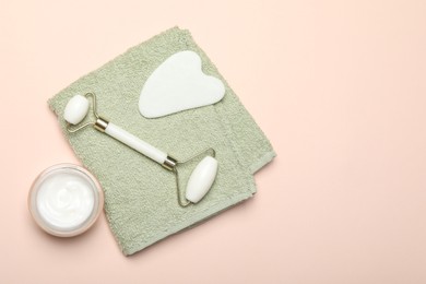 Photo of Face roller, gua sha tool, towel and cosmetic product on beige background, flat lay. Space for text