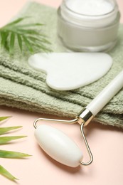 Photo of Face roller, gua sha tool, towel and cosmetic product on beige background, closeup