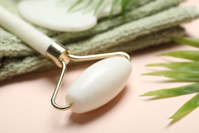 Photo of Face roller, gua sha tool, towel and palm leaves on beige background, closeup