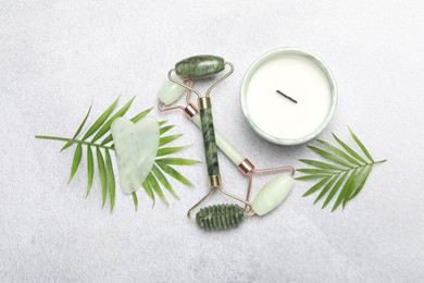 Photo of Face rollers, gua sha tool, scented candle and palm leaves on gray background, flat lay