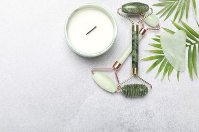 Photo of Face rollers, gua sha tool, scented candle and palm leaves on gray background, flat lay. Space for text