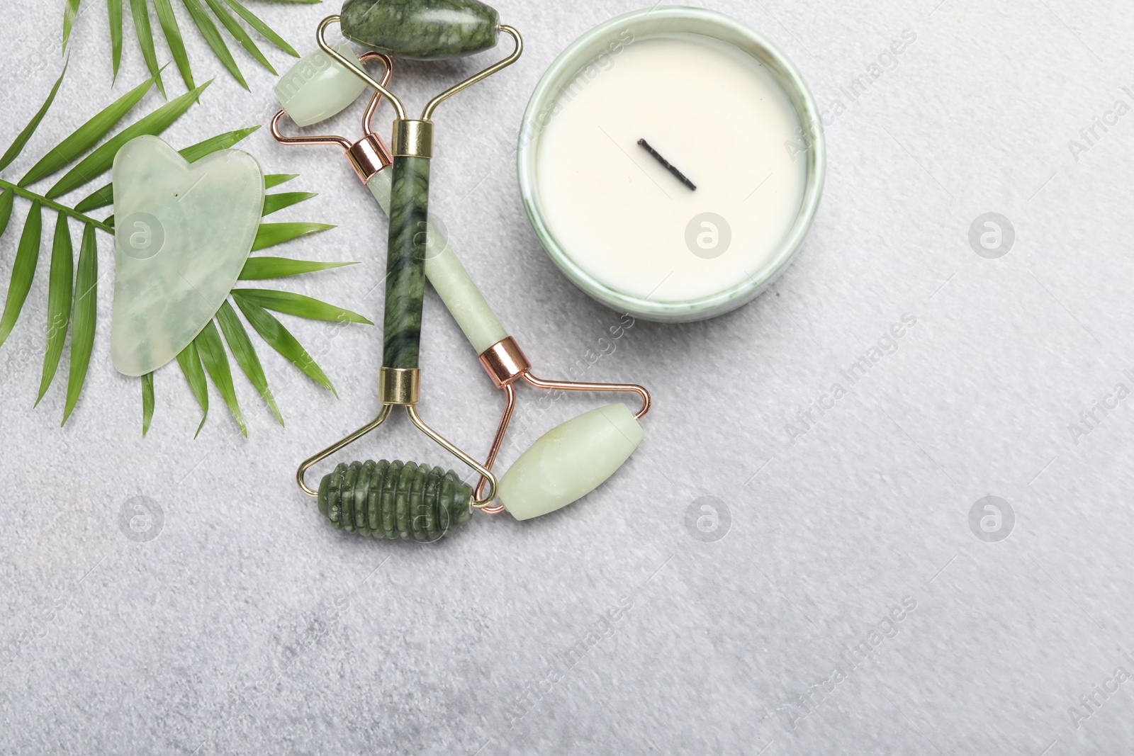 Photo of Face rollers, gua sha tool, scented candle and palm leaves on gray background, flat lay. Space for text