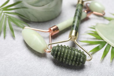 Photo of Face rollers, gua sha tool and palm leaves on gray background, closeup