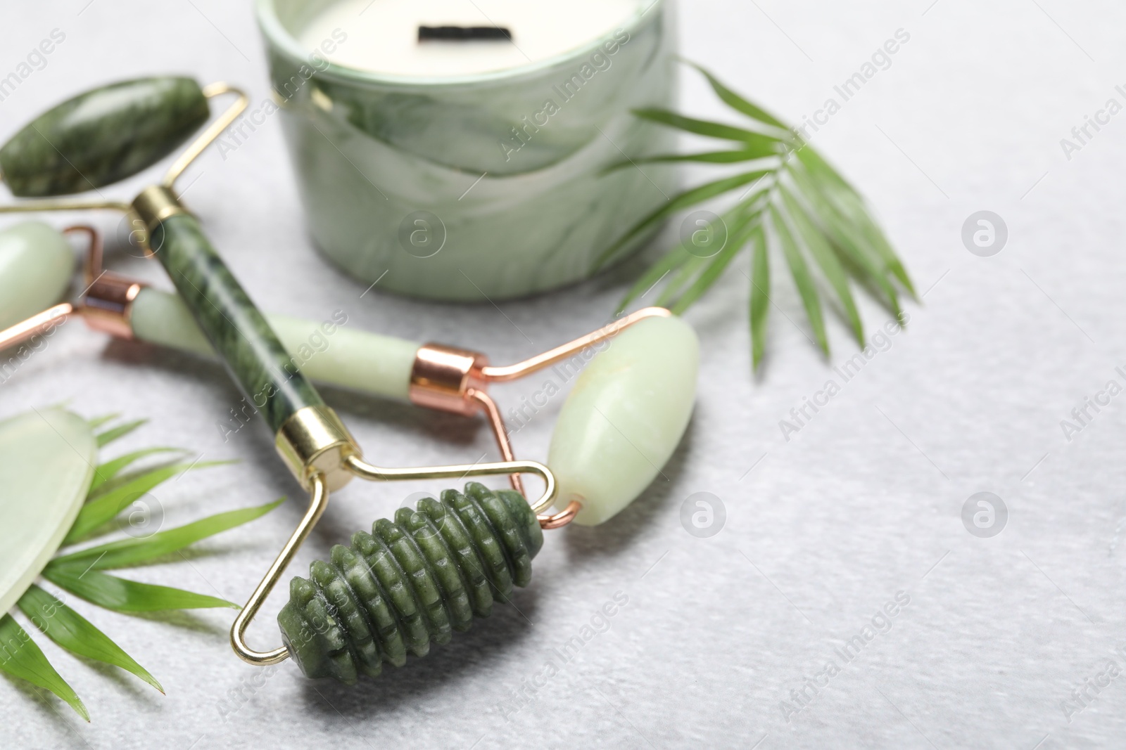 Photo of Face rollers, scented candle and palm leaves on gray background, closeup