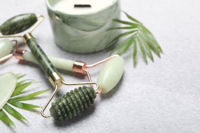 Face rollers, scented candle and palm leaves on gray background, closeup