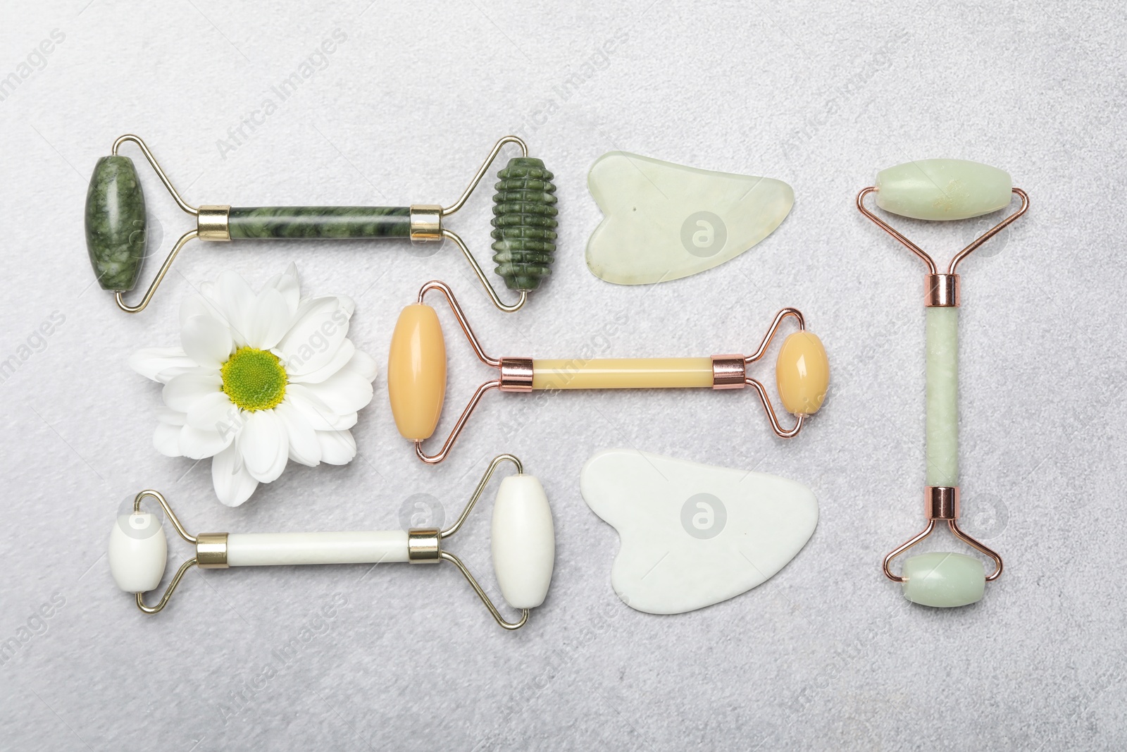 Photo of Face rollers, gua sha tools and chrysanthemum flower on gray background, flat lay