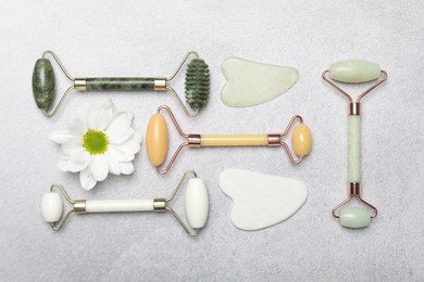 Face rollers, gua sha tools and chrysanthemum flower on gray background, flat lay