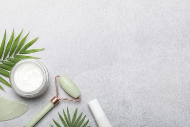 Photo of Face roller, gua sha tool, cosmetic products and palm leaves on gray background, flat lay. Space for text