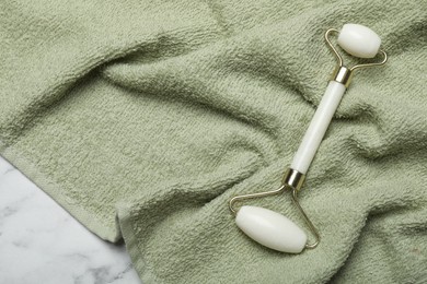 Photo of Face roller and green towel on white marble background, top view