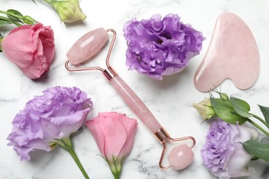 Face roller, gua sha tool and beautiful flowers on white marble background, flat lay