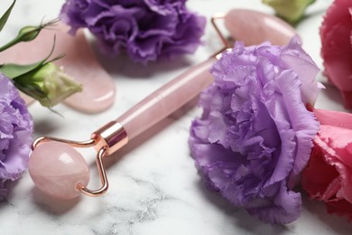 Photo of Face roller, gua sha tool and beautiful flowers on white marble background, closeup