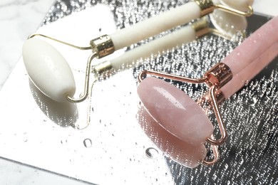 Photo of Face roller with water drops and mirror on table, closeup