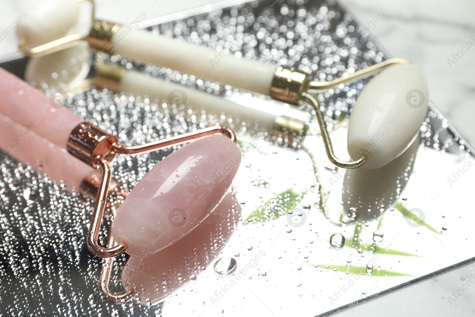 Photo of Face roller with water drops and mirror on table, closeup