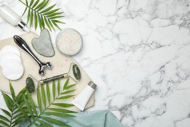 Flat lay composition with face rollers and gua sha tool on white marble background, space for text