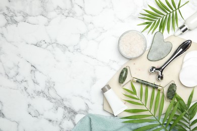 Flat lay composition with face rollers and gua sha tool on white marble background, space for text