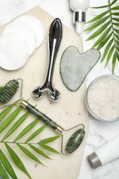 Flat lay composition with face rollers and gua sha tool on white marble background,