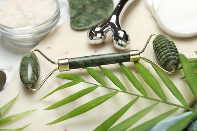 Photo of Face rollers, gua sha tool, sea salt, cotton pads and palm leaves on light background, closeup