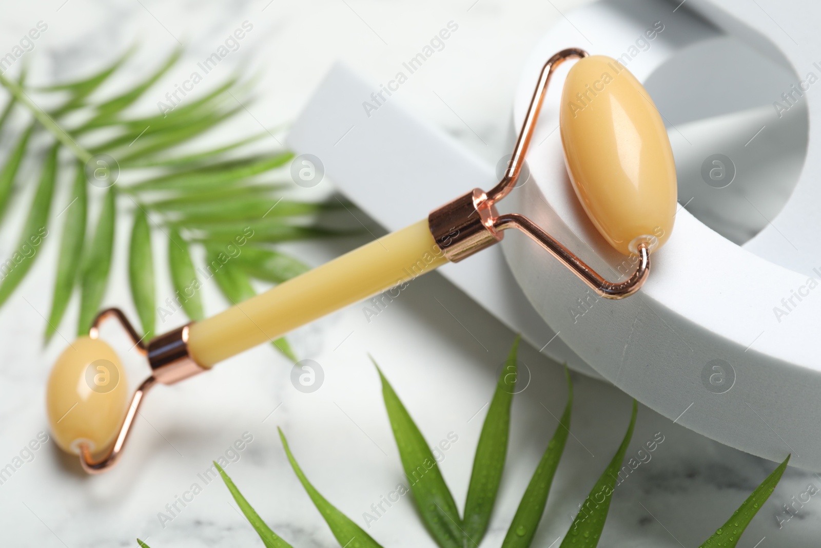 Photo of Face roller and palm leaves on light background, closeup