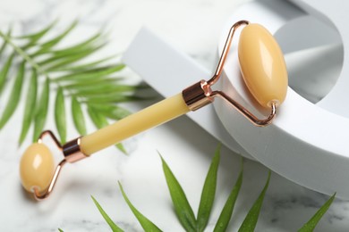 Photo of Face roller and palm leaves on light background, closeup