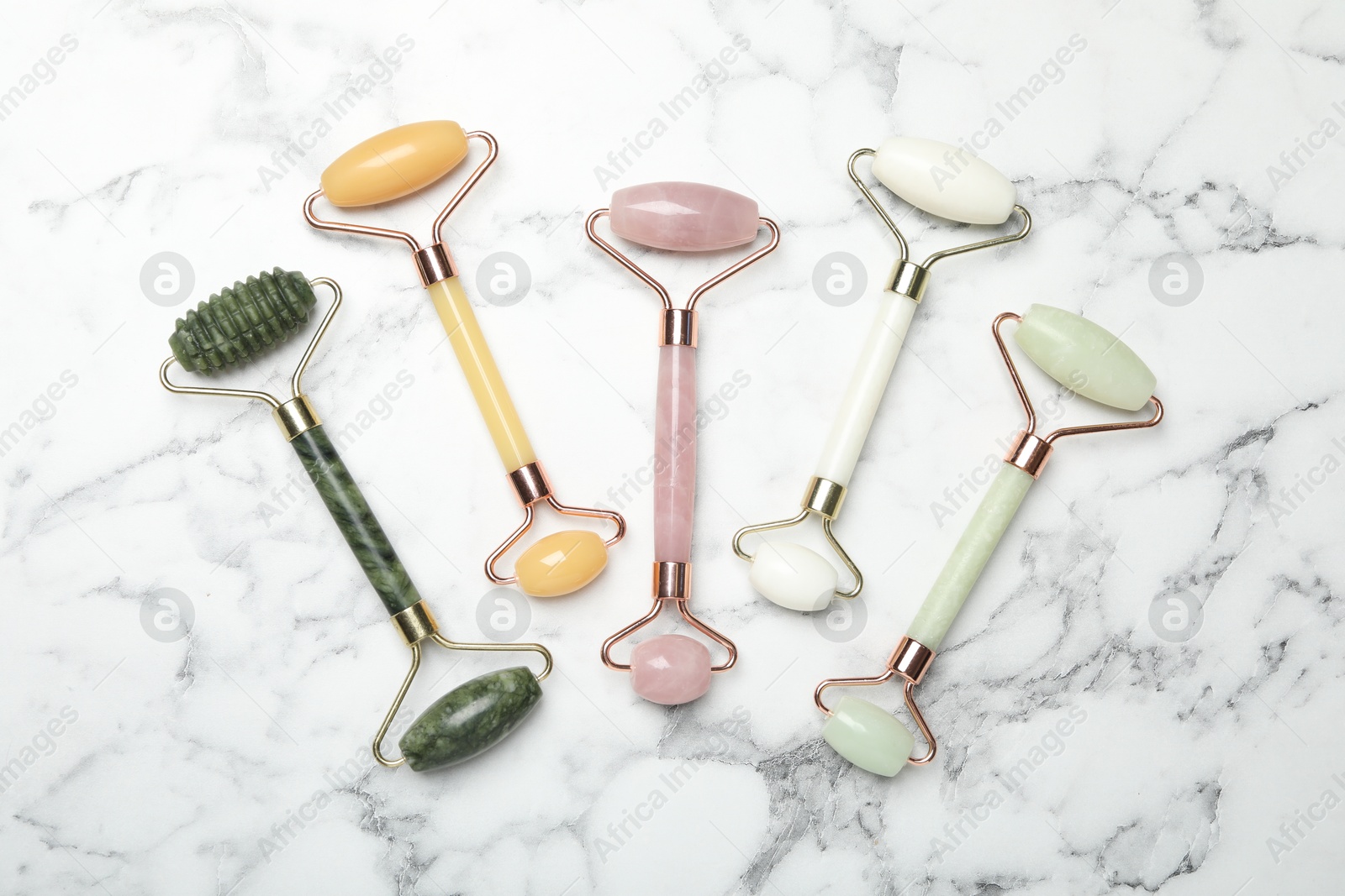 Photo of Face rollers on white marble background, flat lay