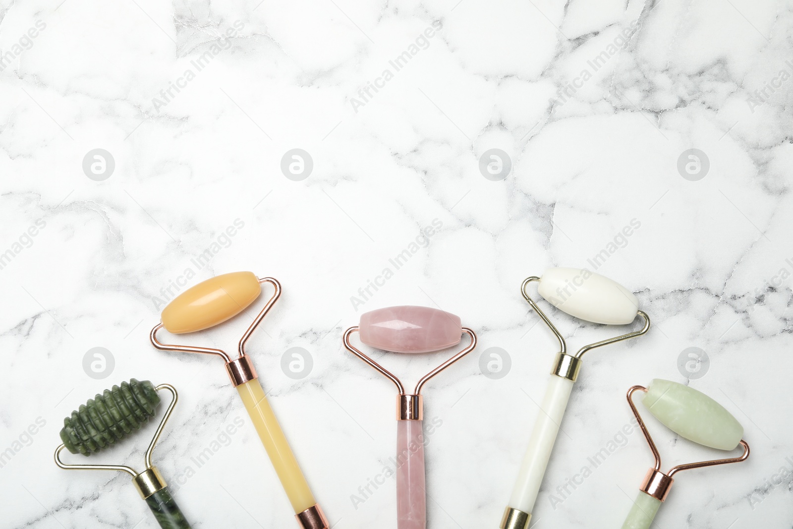 Photo of Face rollers on white marble background, flat lay. Space for text