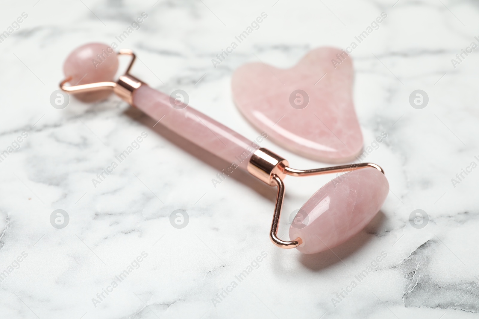 Photo of Face roller and gua sha tool on white marble background, closeup