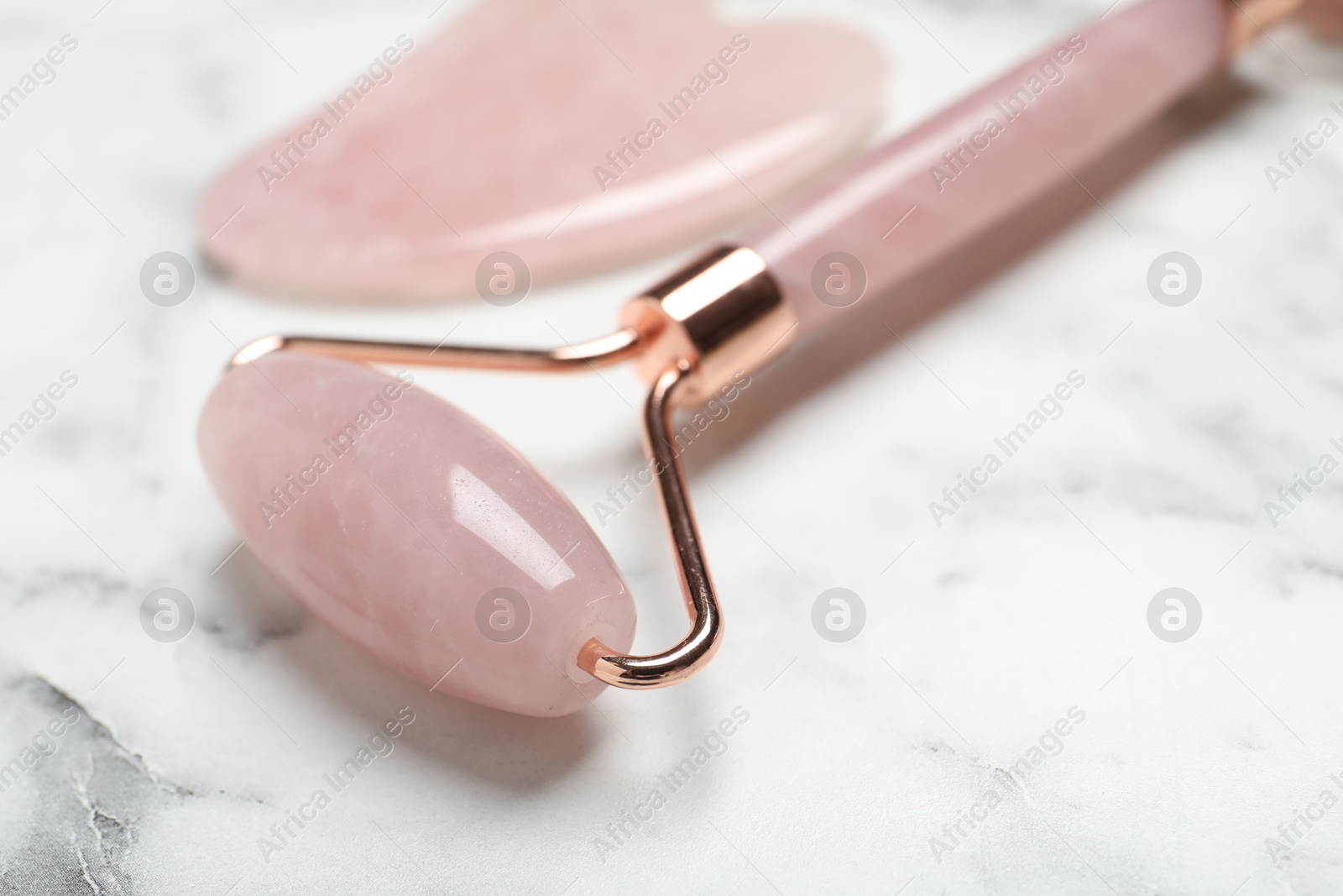 Photo of Face roller and gua sha tool on white marble background, closeup