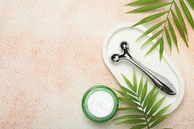 Photo of Metal face roller, cosmetic product and palm leaves on beige textured background, flat lay. Space for text