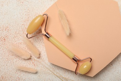 Face roller and dry spikes on beige textured background, flat lay