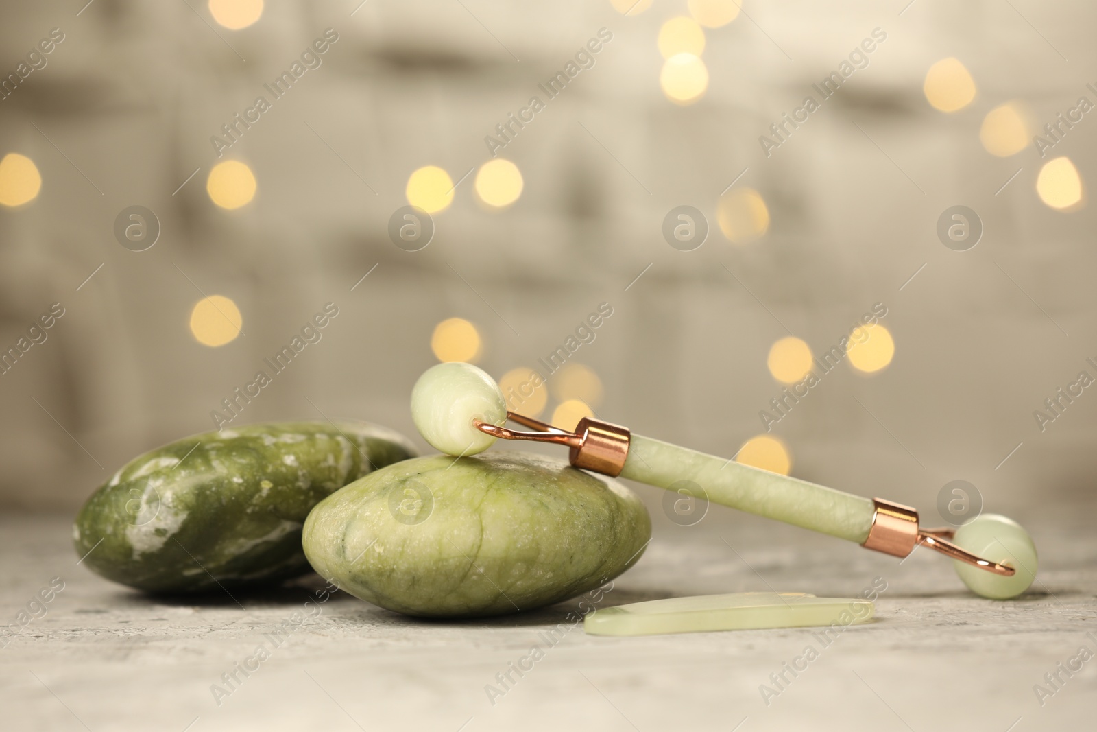 Photo of Face roller, massage stones and gua sha tool, on gray table against blurred lights