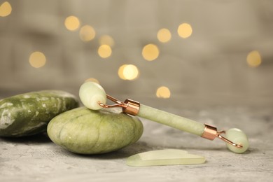 Face roller, massage stones and gua sha tool, on gray textured table against blurred lights, closeup