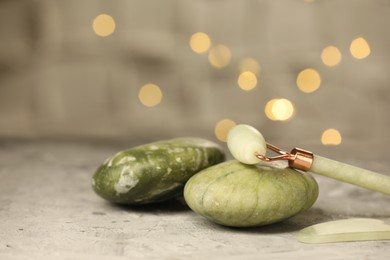 Face roller, massage stones and gua sha tool, on gray textured table against blurred lights, closeup