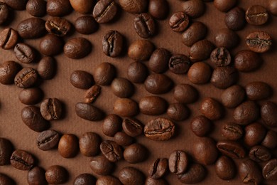 Many coffee beans on brown background, top view