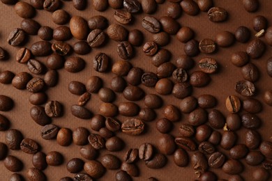 Many coffee beans on brown background, top view