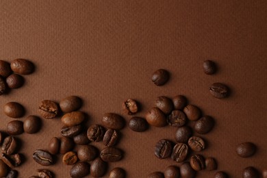 Many coffee beans on brown background, top view